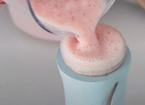 Pink smoothie being poured from a clear blender jar into a light blue portable bottle container.